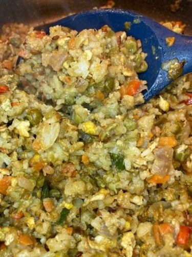 Caribbean styled fried rice with a cooking spoon.