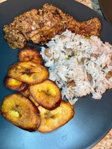 Fried chicken, Jamaican gungo peas and rice, and fried plantains on a dinner plate.