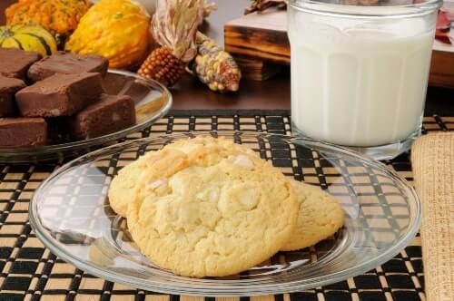 Belgian white chocolate cookies on a clear plate next to milk and fudge squares.